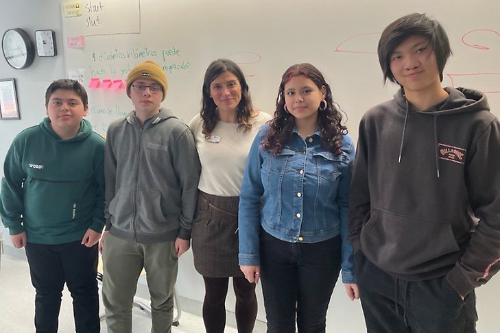 Fyra elever och en lärarinna står framför en whiteboard.