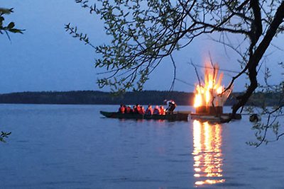 Personer i en låg träbåt tänder en brasa på en flotte ute på en sjö.