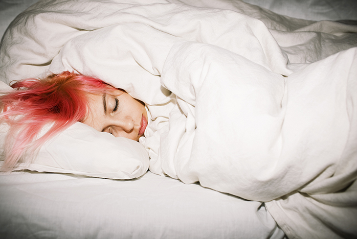 Tonårig tjej med rosafärgat hår sover i säng med vita sängkläder. 