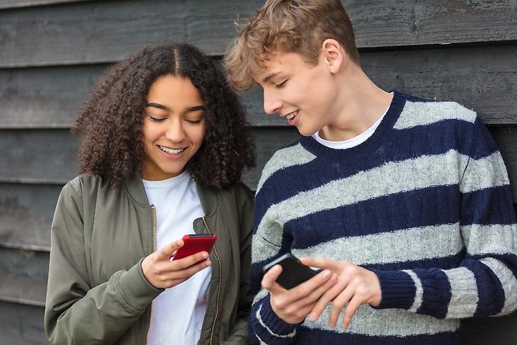 Två tonåringar står med sina mobiler och skrattar.