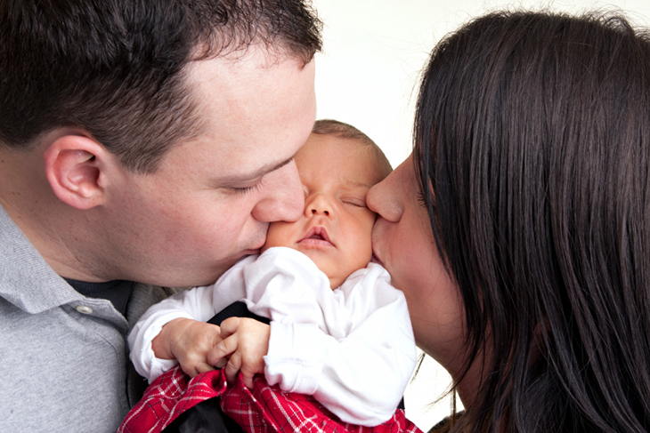 En pappa och mamma pussar sin nyfödda bebis. 
