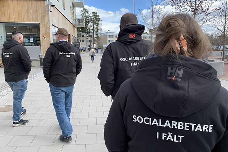 Fyra personer i svarta jackor med texten Socialarbetare i fält på ryggen. De går på ett torg i Valsta centrum.