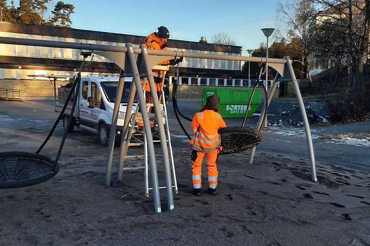 Två personer monterar upp nya stora gungor på en skolgård