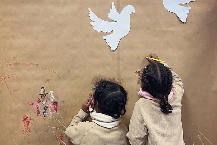 Två flickor sträcker sig mot fåglar i papper som sitter på en vägg