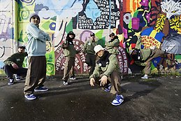 7 killar och tjejer står mot en vägg målad med grafitti