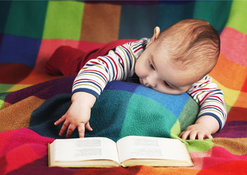 En liten bebis på en röd filt tittar mot en bok