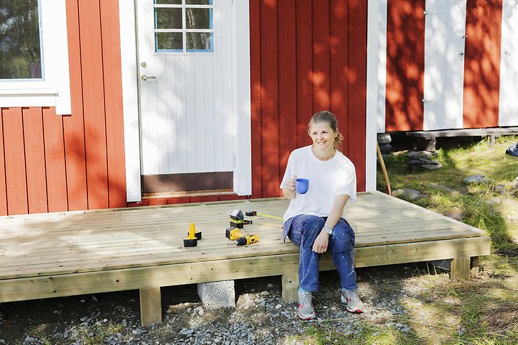 En kvinna tar en kaffepaus på verandan hon håller på att bygga. Fotograf: Bodil Johansson/Johnér 