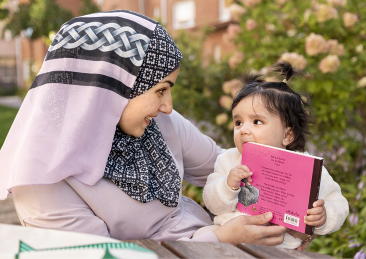 En mamma i hijab håller i ett barn som håller i en bok