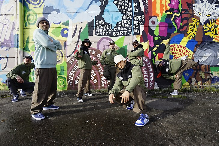 6 personer står mot en graffittimålad vägg